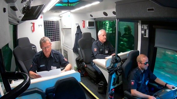 Sicherheitsstufe 1: Drei Justizbeamte überwachen den gesamten Transport der Gefangenen im fahrenden Bus. © NDR/nahaufnahme medienproduktion/Stefan Radüg 