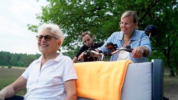 Beim Projekt "Radeln ohne Alter" tritt Martina in der Lüneburger Heide selbst in die Pedale: Marwin Fischer erzählt ihr viel über seine Erfahrung mit begeisterten Seniorinnen und Senioren, die sich in den Rikschas richtig wohl fühlen. © NDR 