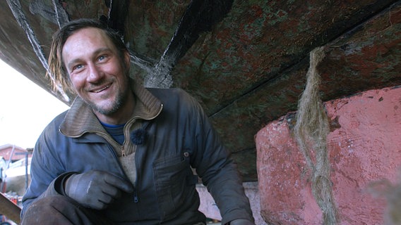 Beim sogenannten Kalfatern, dem Abdichten der Nähte zwischen den Planken, arbeitet Bootsmann Christian mit Hanfgarn und Teer. Beim sogenannten Kalfatern, dem Abdichten der Nähte zwischen den Planken, arbeitet Bootsmann Christian mit Hanfgarn und Teer. © NDR/Joker Pictures