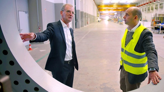 Jürgen Zeschky, Chef des Windradherstellers Enercon vor einem riesiegen Windradbauteil im Gespräch mit NDR Autor Mario Schmidt. © NDR 