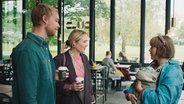 Szenenbild aus der schwedischen Serie "Everyone but us": Drei Personen stehen in einem Cafe und unterhalten sich. © Warner Bros International 