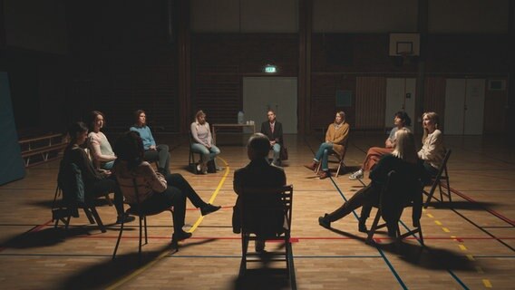 Szenenbild aus der schwedischen Serie "Everyone but us": Eine Gruppe sitzt auf Stühlen im Kreis in einer Sporthalle. © Warner Bros International 