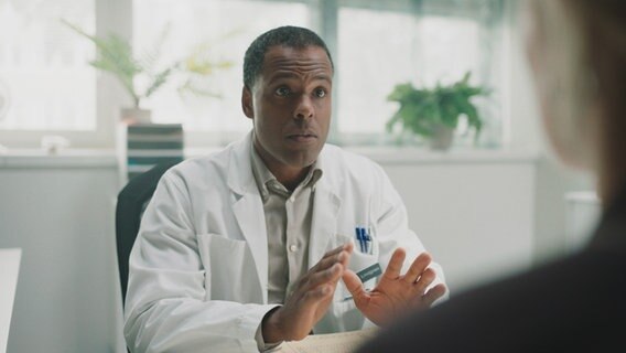 Szenenbild aus der schwedischen Serie "Everyone but us": Ein Mann im Arztkittel sitzt hinter einem Schreibtisch. © Warner Bros International 