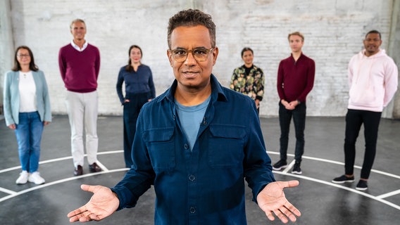 Wie egoistisch bist du? Moderator Michail Paweletz und die sechs Teilnehmenden in einer ehemaligen Lagerhalle in Hamburg. (v.l.n.r.: Mitra Kassai, Jörg von Grass, Julia Breckheimer, Priyanka Balamohan, Johannes Kolb, Rene Mang) © NDR/Stefan Mühlenhoff 
