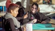 Zwei Jugendliche sitzen an einem Tisch im Klassenraum und beschreiben ein Plakat. © NDR 