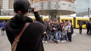 Eine Frau fotografiert eine Gruppe von Jugendlichen auf dem Alexanderplatz in Berlin. © NDR 