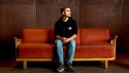 Der YouTuber Philipp Mickenbecker sitzt auf einem Sofa. © NDR 