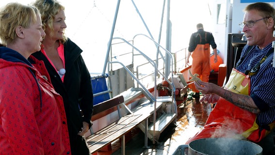 Bettina Tietjen und Mirja Boes lassen sich von einem Krabbenfischer den Beifang erklären. © NDR/beckground tv/Marvin Vehring 