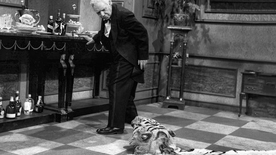 Freddie Frinton als Diener James und May Warden als alleinspeisende alte Dame. Diener James stolpert über das Tigerfell. © NDR/Annemarie Aldag 