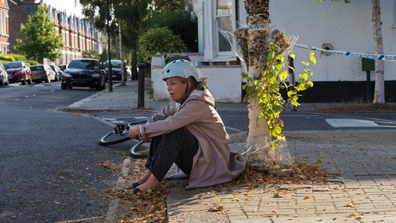 Szenenbild aus der Serie "The Split - Beziehungsstatus ungeklärt": Eine Frau mit Fahrradhelm sitzt an der Bordsteinkante. © NDR/Sister Pictures Foto: Tereza Cervenova