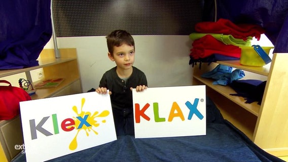 Ein junge zeigt zwei Schilder mit den Namen Klex und Klax  