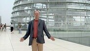 Ein Mann breitet die Arme vor der Reichstagskuppel aus.  