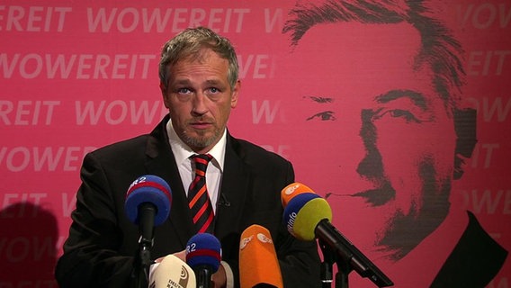 Der Schriftsteller Torsten Sträter vor einem rosafarbenen Plakat, das Klaus Wowereit zeigt.  