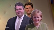 Christian Ehring schaut hinter Pappaufstellern von Merkel und Gabriel hervor.  
