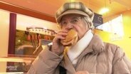 Eine Oma beisst in ein Brötchen.  
