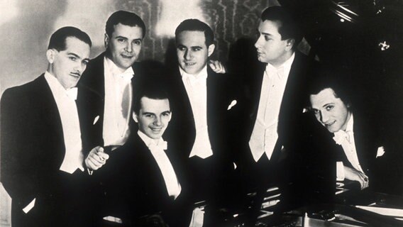 Die Comedian Harmonists in ihrer Originalbesetzung stehen in Fräcken um einen Flügeln: von links: Ari Leschnikoff, Erich Abraham-Collin, Roman Cycowski, Robert Biberti, (halb gebückt), Harry Frommermann-Frohman, (sitzend) Erwin Bootz. © NDR 