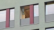 Ein offenes Bürofenster in einer grünen Häuserfassade.  
