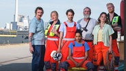 Darstellerinnen und Darsteller der Miniserie "Festmachen" posieren im Hafen für die Kamera: Karsten Antonio Mielke, Nina Petri, Nils Rovira-Munoz, Salka Weber, Jochen Nickel, Meryem Ebru Öz und Peter Plaugborg. © Iris Janke/Leitwolf/Katharina Rival 