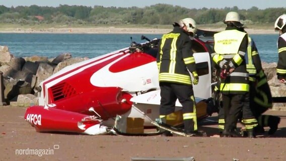 Feuerwehrleute begutachten Teile eines abgestürzten Hubschraubers.  