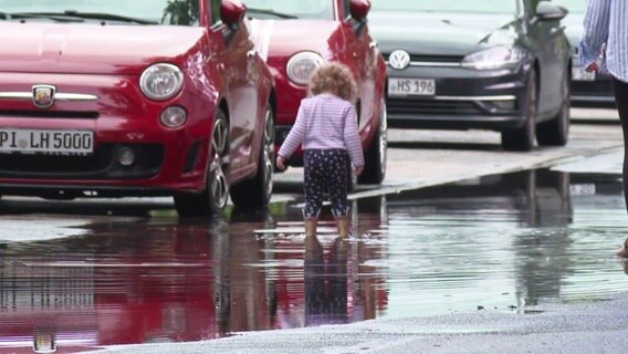 Ein kleines Kind spielt auf einer überfluteten Straße. © NDR Foto: Screenshot
