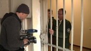 Ein Reporter steht in einer Gefängniszelle.  