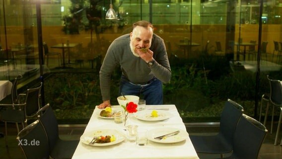 Ein Mann isst stehend an einem Tisch  