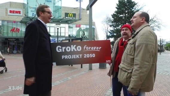 Zwei Männer halten eine Werbeschild für die GroKo  