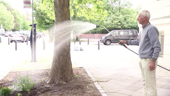 Ein Mann gießt eine öffentliche Grünfläche.  