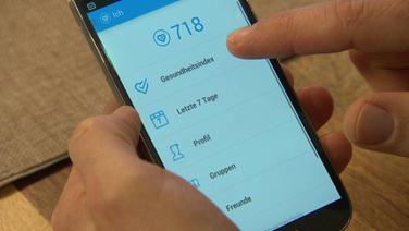eine Hand zeigt auf ein Handy mit der App "Gesundheitsindex"  