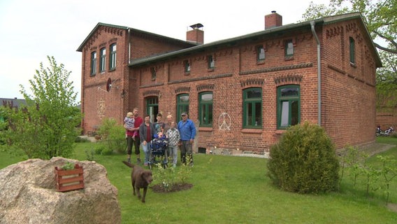 Eine Familie vor einem Rotklinkerhaus im Grünen.  