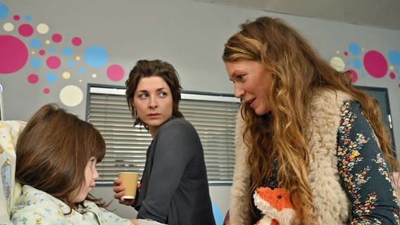 Eva Steeger (Katharina Nesytowa, M.) und ihre Frau Chris Steeger (Rebecca Rudolph, r.) freuen sich, dass es ihrer Tochter Emily Steeger (Kleindarstellerin), die eine Vergiftung erlitten hat, wieder besser zu gehen scheint. © ARD/Hardy Spitz 