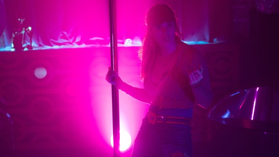 Szenenbild aus der französischen Serie "HIP: Ermittlerin mit Mords-IQ": Eine Frau tanzt an einer Stange im pinkfarbigen Licht. © François Roelants Foto: François Roelants