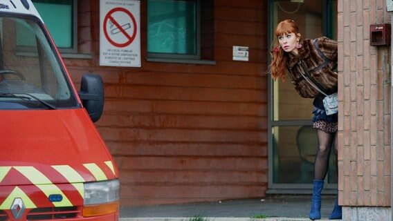 Szenenbild aus der französischen Serie "HIP: Ermittlerin mit Mords-IQ": Eine Frau guckt um eine Hausecke. © Nicolas Gouhier Foto: Nicolas Gouhier
