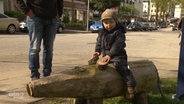 Ein kleines Kind sitzt auf einem Schwein aus Holz.  