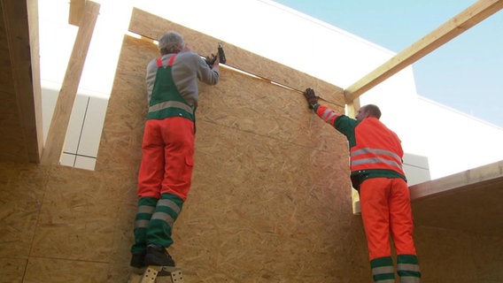 Zwei Arbeiter bauen eine Holzwand auf  