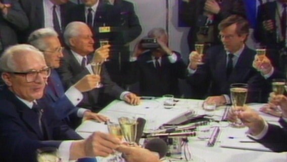 Honecker stößt in einer Tischrunde mit Sekt an.  