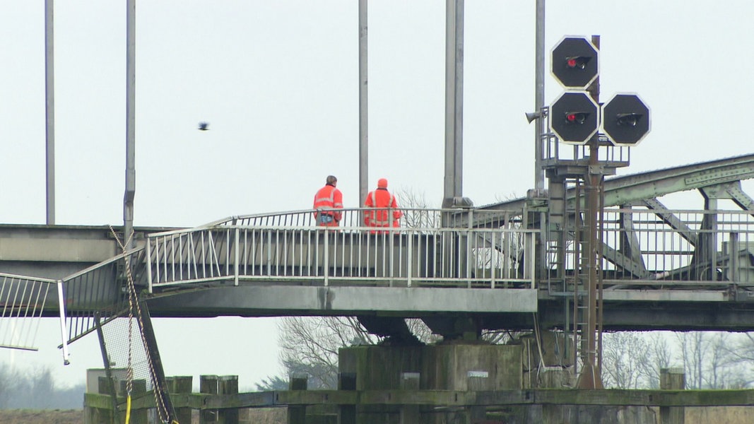 Zwei Personen in Signal-Arbeitskleidung stehen auf der beschädigten Eisenbahnbrücke über die Hunte.