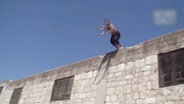 Ein Mann springt von einem Hausdach.  