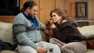 Szenenbild aus der Impro-Serie "Kranitz - Bei Trennung Geld zurück": Ein Paar sitz mit einem Hund auf einem Sofa. © ARD Degeto/NDR/Thomas Leidig 