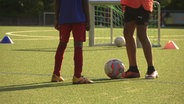 Zwei Jugendliche spielen Fußball auf einem Kunstrasenplatz  