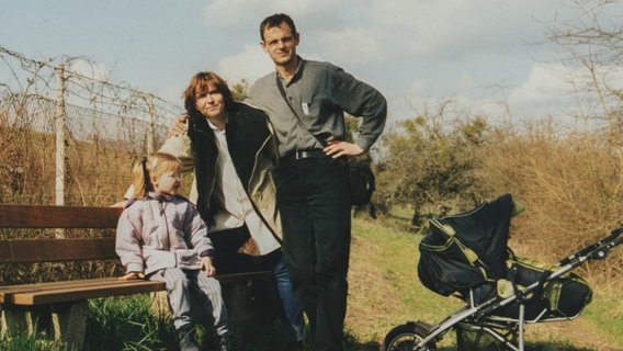 Szene aus Kurzzeitschwester: Auf einer Bank in der Natur aufgenommenes Familienfoto der Eltern des Autoren mit der kleinen Adoptivtochter. © NDR/DRIVE beta GmbH/Philipp Lippert 