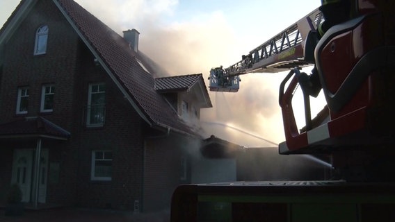 Ein verqualmtes Einfamilienhaus wird von einem Feuerwehrmann auf einer Drehleiter gelöscht. © Nord-West-Media TV 