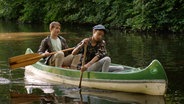 Lisha und Johannes sitzen in einem Boot auf dem Wasser.  