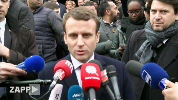 Emmanuel Macron ist umringt von vielen Mikrofonen.  