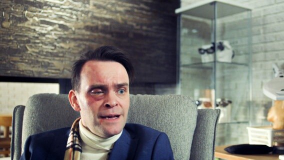 Ein Mann mit lädiertem Gesicht sitzt im Sessel. © NDR/Viafilm AS 