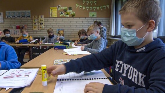 Blick in eine Grundschulklasse, in der die Kinder jeweils eine Maske über Mund und Nase tragen.  