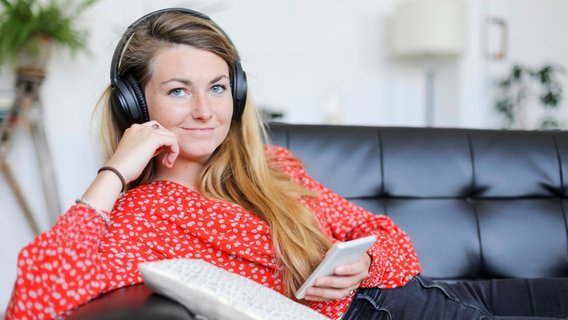 Eine junge Frau auf einem Sofa hört Musik über das Handy © Photocase Foto: 2Design