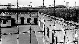Blick durch Stacheldraht auf Gebäude des Konzentrationslagers der SS im tschechischen Theresienstadt, undatierte Swarzweiß-Aufnahme. © picture alliance / dpa-Bildarchiv 