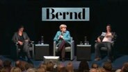 Angela Merkel auf einem Sofa sitzend (Videocollage).  