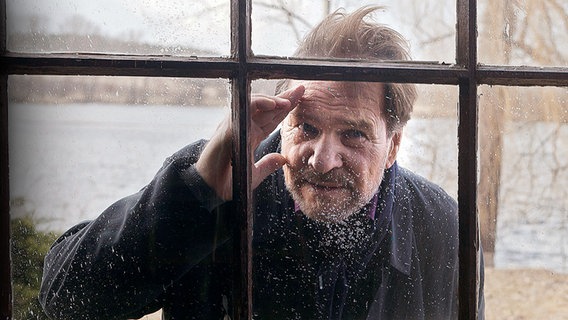 Jasper Dänert (gespielt von Götz George) schaut durch ein Fenster in das Innere eines offenbar heruntergekommenen Hauses. Er ist ein Mann mit Scheitelfrisur und gepflegten Bart. © WDR/Erik Lee Steingroever 